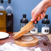 A hand holds a wooden dumpling press tool over a round wooden base on a cutting board.