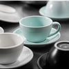 A close-up shot of light blue ceramic latte cups and saucers on a dark surface.