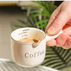 A hand holds a single-handle ceramic coffee cup with a handle, demonstrating its design for a comfortable hand feel.