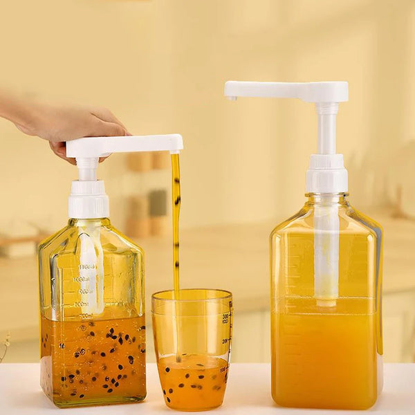 A hand is dispensing orange syrup from a white pump dispenser bottle into a glass.