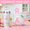 A white tumbler decorated with a pink glitter letter A and a pink charm, shown on a red and white checkered tablecloth.