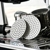 A close-up of a stainless steel reusable espresso filter for a portafilter resting on a machine surface.