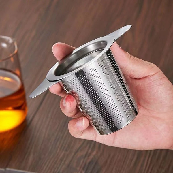 A hand holds a stainless steel coffee filter funnel with a lid, showing the perforated metal design.