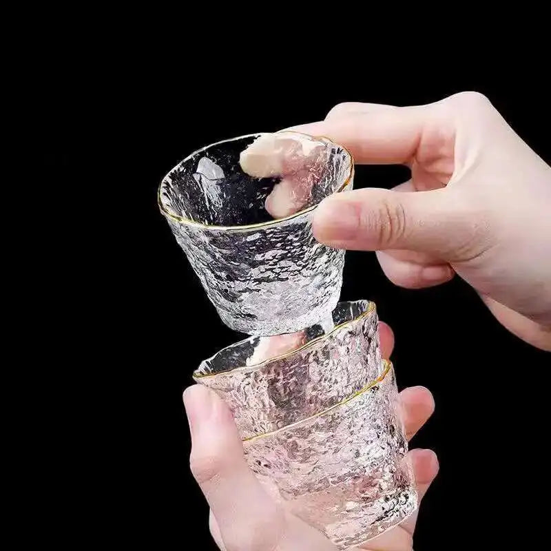 A hand is holding a delicate glass tea set for Chinese and Japanese ceremony, showing two nested glass cups.
