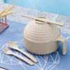 A beige microwave ramen cooking set with a lid and utensils resting on a blue cloth.