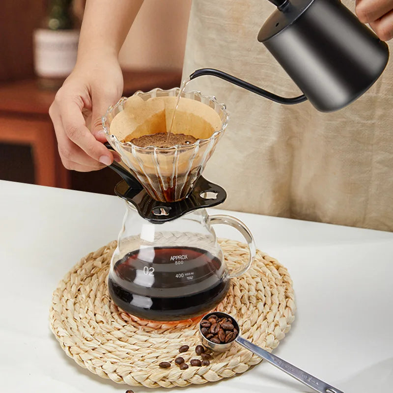 A hand pours coffee into a glass dripper over a ceramic mug, demonstrating a manual pour over coffee brewing process.