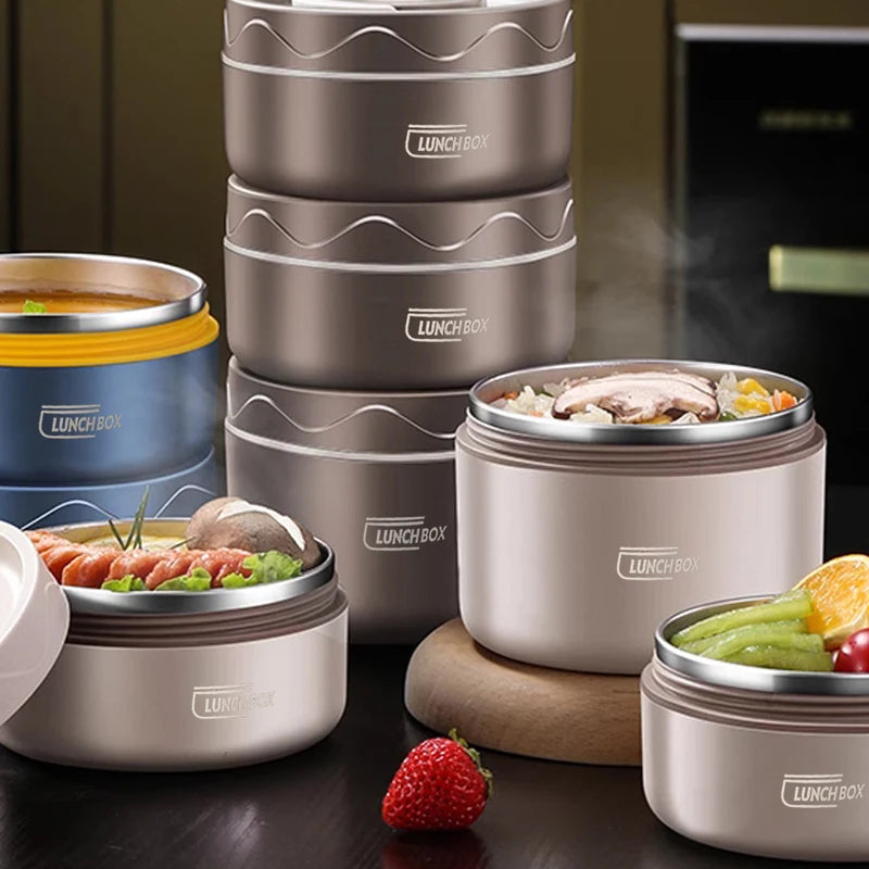 A stack of stainless steel insulated lunch boxes in various shades of beige and blue are displayed on a dark surface.