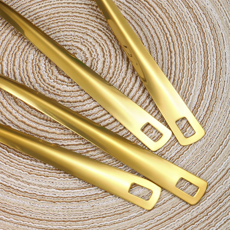 A pair of golden stainless steel soup spoons and a colander resting on a beige woven surface.