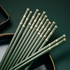A set of chopsticks with gold accents is displayed diagonally on a dark green surface.