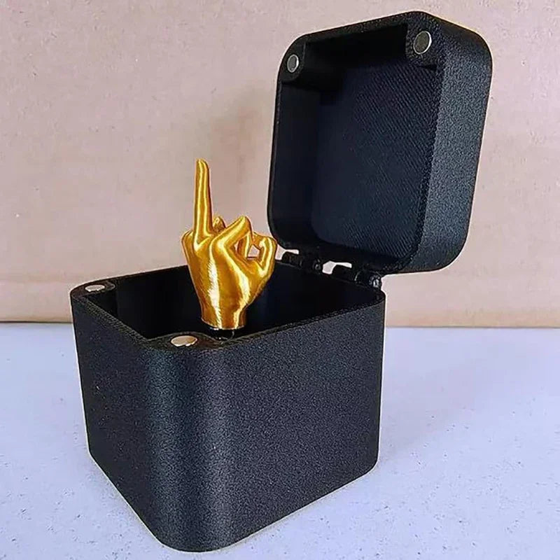 A black gift box with an open lid displaying a golden hand making the middle finger gesture.