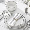 A white ceramic dinnerware set featuring plates, bowls, and silverware arranged on a white marble surface.