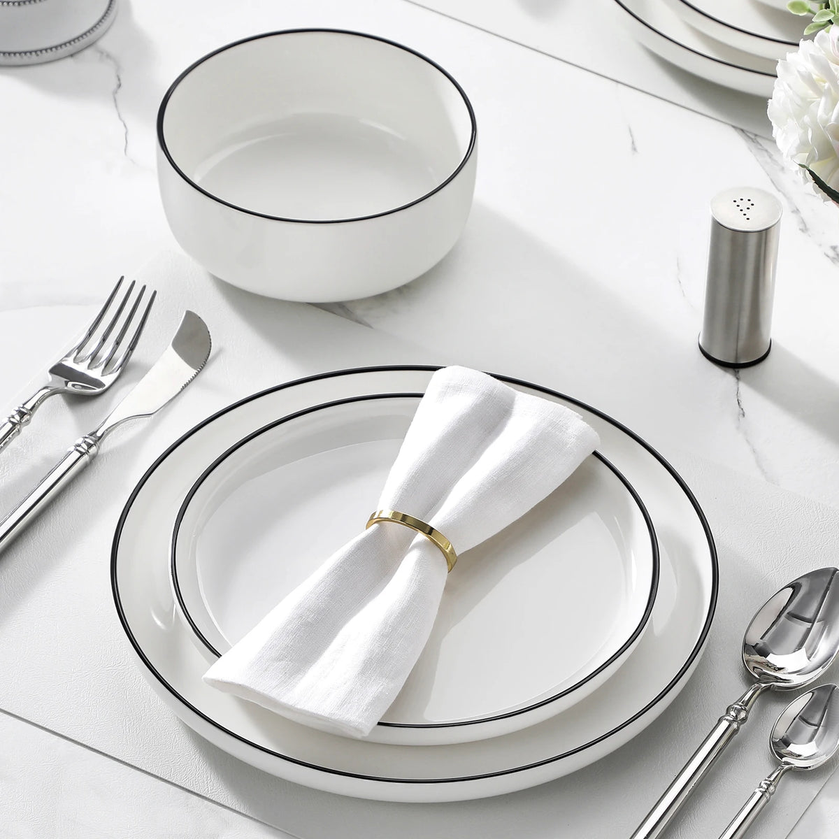 A white ceramic dinnerware set featuring plates, bowls, and silverware arranged on a white marble surface.