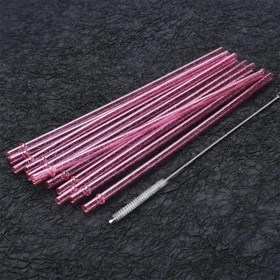 A bundle of pink glitter reusable plastic straws with cleaning brushes laid diagonally on a black surface.