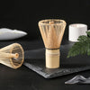 A set of natural bamboo tea tools, including a funnel-shaped item and a round sieve, displayed on a dark surface.