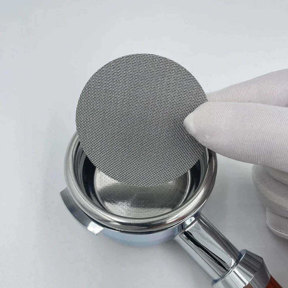 A hand is placing a perforated metal filter plate replacement onto a silver coffee filter holder.