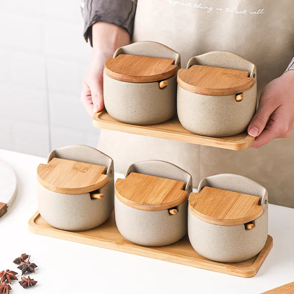 A set of ceramic seasoning jars with bamboo lids displayed on a wooden tray.