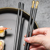 A pair of black chopsticks with gold accents are held over a gray plate next to sushi.