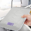 A hand places a silver digital kitchen scale on a countertop, showing the display reading 19 grams.