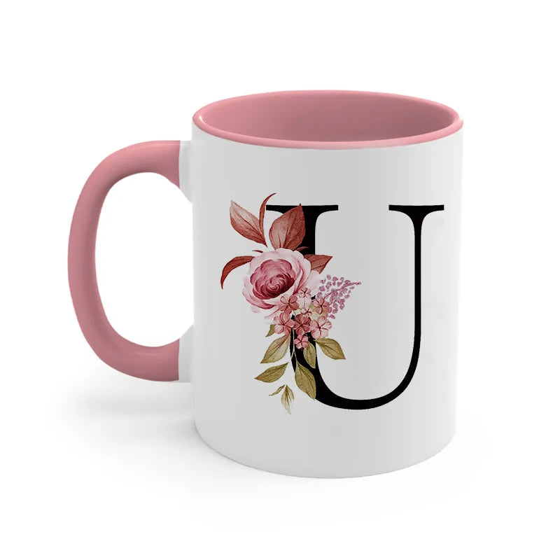 A pink coffee mug with a large black letter U monogram decorated with pink and green floral designs.