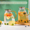 A large glass water pitcher filled with fruit and water, featuring a metal lid and handle.
