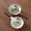 A silver stainless steel tea strainer filter with a wooden handle resting on a brown wooden surface.