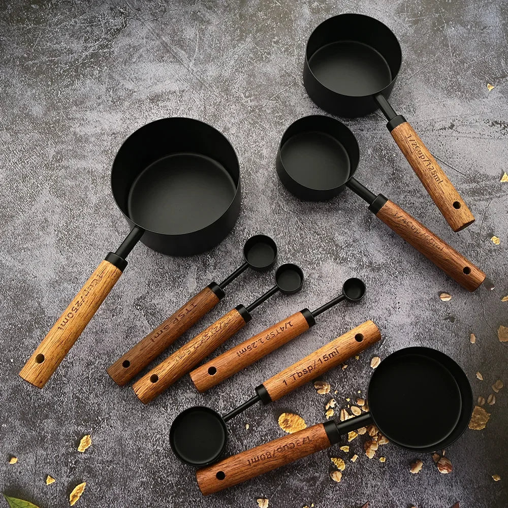 A set of stainless steel measuring spoons with wooden handles scattered on a gray surface.