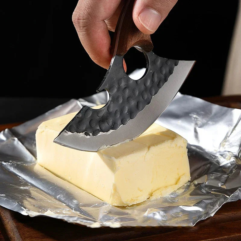 A hand is using a heavy-duty utility cleaver knife with a wooden handle to cut a block of butter on aluminum foil.