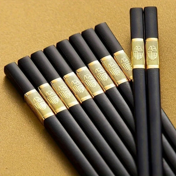 Ein Set wiederverwendbare schwarze Glasfaser-Stäbchen mit goldenen Akzenten, diagonal auf goldenem Hintergrund.