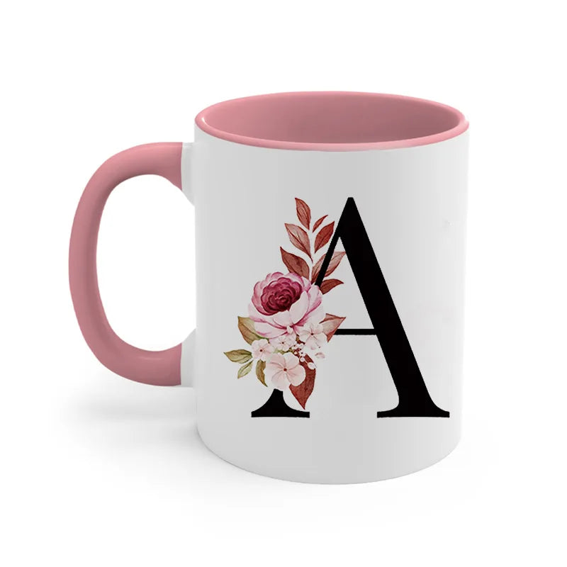 A pink coffee mug with a large black letter A decorated with floral elements.