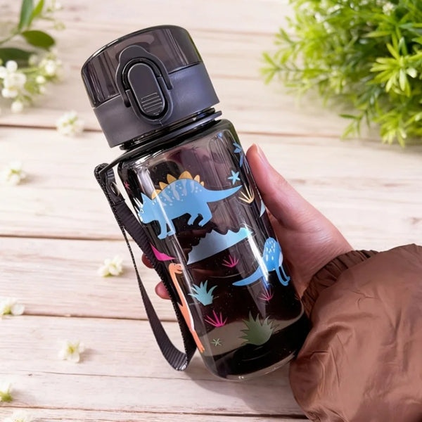 A hand holds a dark plastic water bottle with a dinosaur pattern against a light wooden background.