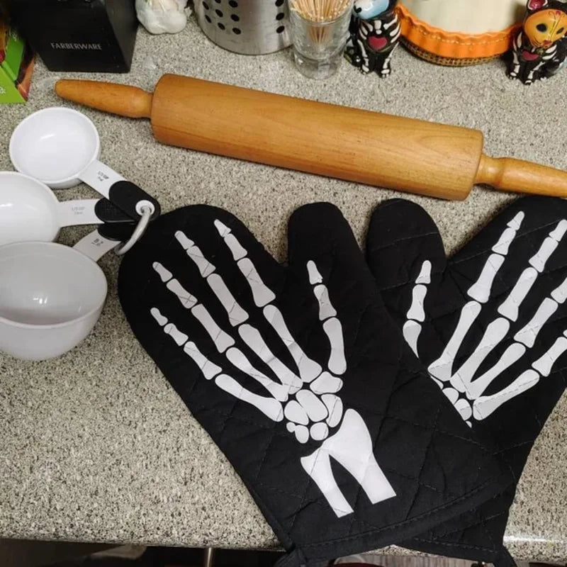 A set of black oven mitts featuring white skeleton hand designs and a wooden rolling tool are displayed on a countertop.