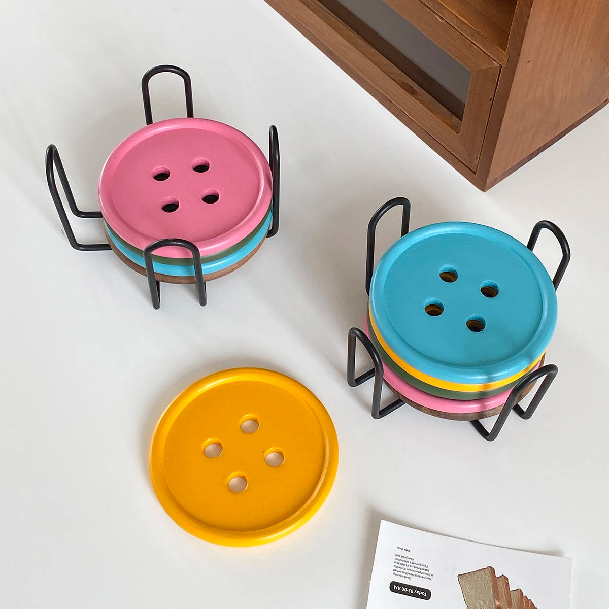 A set of three colorful wooden coasters, pink, blue, and yellow, with iron racks.
