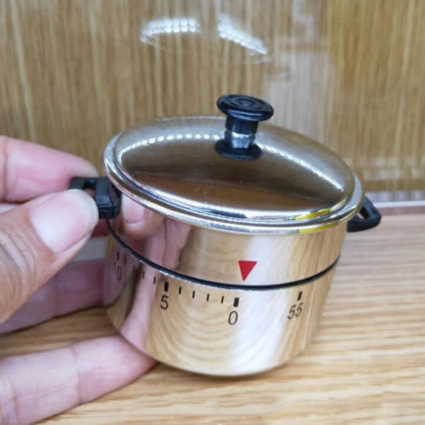 Eine Hand hält einen silbernen mechanischen Küchenwecker mit Holzgehäuse und schwarzem Deckel, der die Messskala zeigt.