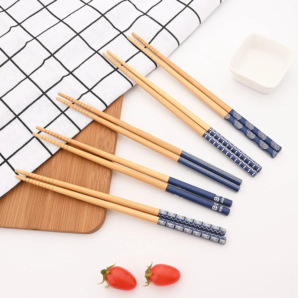 A set of reusable bamboo chopsticks with blue and white patterned tips resting on a white dish and a wooden board.