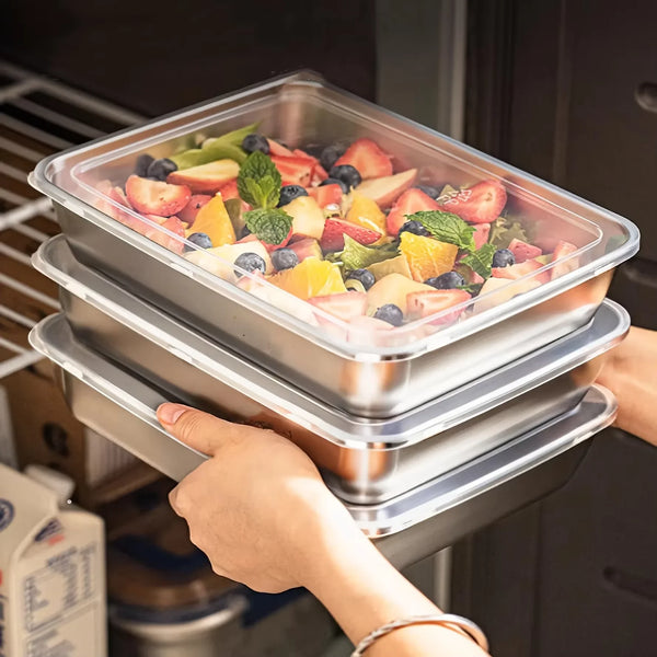 Eine Hand hält einen durchsichtigen Plastikbehälter mit gemischten Früchten und Gemüse in einer Stapel aus Edelstahlcontainer